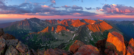 An aerial view depicts a mountain range with peaks illuminated by golden light. The scene features dynamic cloud formations and a gradient sky with shades of pink, blue and orange. This landscape photography is suitable for various commercial applications such as travel brochures or environmental campaigns.の素材