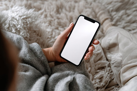 A person is holding a smartphone with a blank white screen, suggesting screen content placement. The scene features a soft, textured background with neutral colors. The composition includes close-up details, potentially suitable for advertising, marketing, or website design mockups. Soft natural lighting suggests an indoor setting.の素材