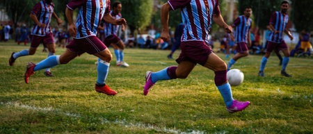 A group of soccer players are running on a green grass field. They are wearing matching uniforms. The composition captures motion. Sunlight illuminates the scene. This image could be utilized for athletic, sports, or health related projects. It showcases teamwork and competitive play.の素材