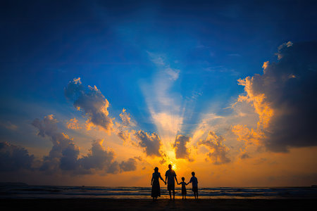 A family stands on the shore silhouetted against a vibrant sunset. The image showcases a dynamic composition with dramatic lighting and warm colors. This photograph may be suitable for commercial use in various editorial contexts, conveying themes of togetherness and leisure activities.の素材
