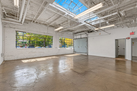 An empty industrial interior is shown with a concrete floor and white walls. Sunlight streams through large windows and skylights, illuminating the space. The composition highlights architectural details, and provides copy space. This image is suitable for commercial and design applications.の素材