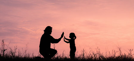 This image features the silhouette of a parent and child giving each other a high five. The composition is set against a gradient pink sky. The scene suggests an outdoor setting. The image's simplicity allows for use in various projects, from commercial illustrations to editorial content.の素材