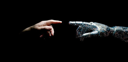 A human hand and a robotic hand almost touching are depicted in a dramatic, low-key setting against a black background. The composition highlights the contrast between organic and artificial. The image features dark tones and strong directional lighting, potentially suitable for various technological and conceptual themes.の素材