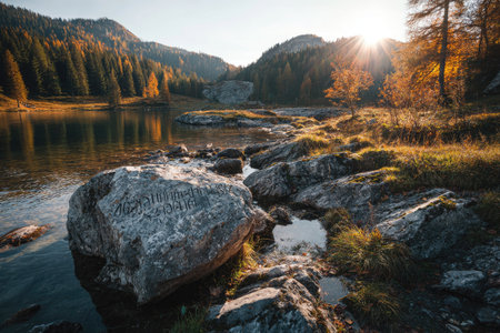 A scenic view showcases a serene lake surrounded by rocks and trees in autumn colors. The composition features sunlight illuminating the scene, highlighting textures. The image suggests a peaceful atmosphere. Suitable for travel, nature, and environmental concepts, it offers versatility for various visual projects.の素材
