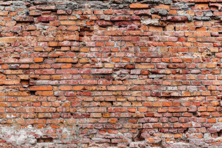 An aged brick wall presents a textured surface with visible wear and tear. The composition displays a mix of red and brown bricks with varied patterns and color variations. The image captures an overhead view, suggesting an outdoor setting. Suitable for various design and advertising applications.の素材