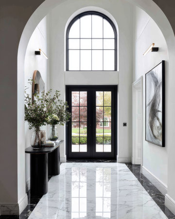A high-angle shot displays a well-lit hallway with a glossy marble floor leading towards a set of black double doors and a large arched window. The space features black accents, including a console table and door frames, and a contemporary art piece. This image is suitable for various interior design and architectural projects.の素材