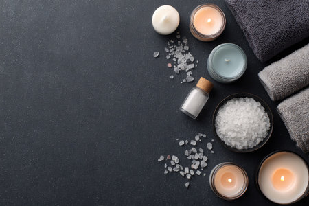 This overhead view showcases a spa arrangement featuring candles, towels, and bath salts. The composition uses a dark color palette, highlighting the textures of the items. Soft lighting from the candles illuminates the scene, suggesting a relaxing environment. This image is ideal for use in wellness and lifestyle publications.の素材