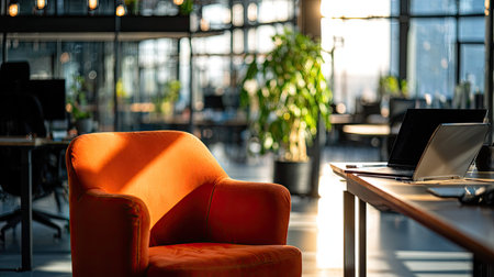 An interior shot reveals a modern office setting. The foreground features an orange armchair. Natural sunlight illuminates the space. The composition includes desks with laptops and potted plants. The blurred background suggests a larger workspace environment suitable for commercial use.の素材