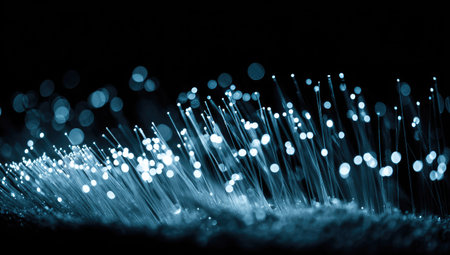This image showcases a close-up of fiber optic strands emitting glowing light. The composition features a dark background with blurred, round highlights. The overall aesthetic is futuristic and technical, suitable for visualizing concepts related to communication and data transmission. This image could be used in various commercial and editorial contexts.の素材