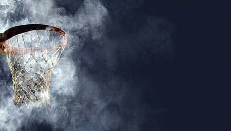 An aged basketball hoop with a tattered net is framed against a deep, dark backdrop. The scene is enveloped in a swirling, smoky haze, creating a dramatic atmosphere. This image could be used for various projects, emphasizing sports, competition, or artistic concepts, suitable for editorial or commercial applications.の素材