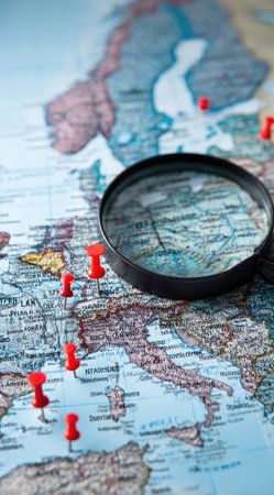 A detailed map with red push pins is viewed through a magnifying glass. The image exhibits a textured surface with diverse colors and geographical details. The composition suggests travel, exploration, and planning. Suitable for illustrating concepts related to international relations or commercial endeavors.の素材