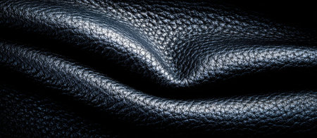 This image showcases a close-up of a dark leather surface, displaying intricate textures and folds. The play of light and shadow highlights the material's rich details. The composition may be suitable for advertising, design projects, and visual content creation. It evokes a sense of luxury and depth.の素材