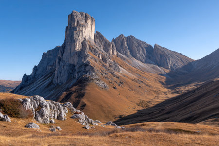 This image showcases a striking mountain range under a brilliant blue sky. The scene is dominated by massive, textured rock formations. Warm, earthy tones of the landscape contrast with the clear sky. This image could be used for various projects needing visuals of nature, travel, or exploration.の素材