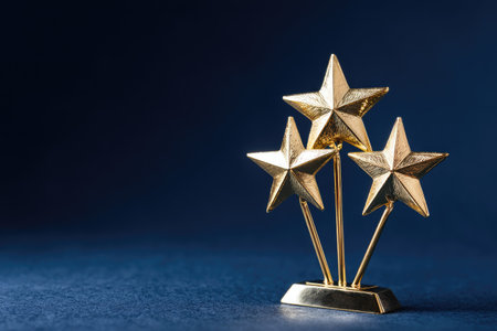 Three gold stars stand prominently against a deep blue backdrop. The metallic figures are lit to emphasize their shape. The image displays a balanced composition. It could be used in projects about recognition, leadership, or success. The photograph's simplicity is ideal for commercial or editorial applications.の素材