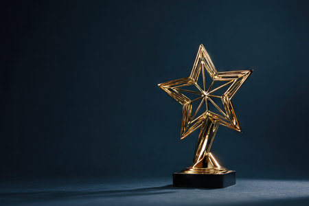 A golden star award trophy stands prominently against a dark blue backdrop. The object has intricate geometric patterns and a shiny metallic texture. The composition utilizes low-key lighting to emphasize the award's form. It may be suitable for promotional materials or editorial content related to achievement.の素材