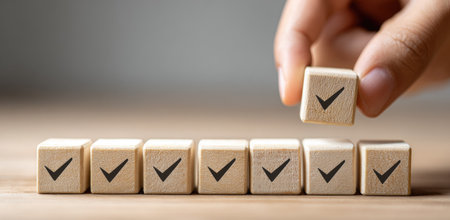 A hand places a wooden block with a check mark onto a row of similar blocks. The blocks are arranged on a wooden surface. The image exhibits neutral tones, and simple composition. It is suitable for various commercial purposes, including illustrations related to decisions or completion.の素材