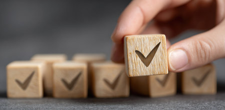 A hand carefully holds a wooden cube displaying a check mark, highlighting a symbol of selection and agreement. The composition features a shallow depth of field, with other cubes in soft focus. This image could be suitable for various commercial or editorial applications such as business, education, or decision-making.の素材
