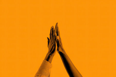Two hands reach towards the top of the frame against a flat orange backdrop. The composition features high-contrast lighting and a monochrome palette. This image could be used for various purposes, including editorial content or as an element in design projects and marketing materials.の素材