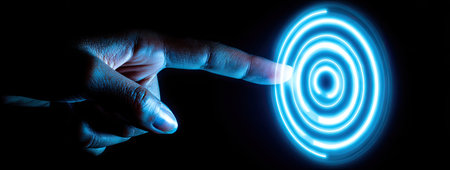 A hand is reaching towards a series of glowing blue concentric circles. The image features high-contrast lighting and a dark background, highlighting the blue light. This visual concept represents interaction, innovation, and digital transformation, suitable for use in technology and business contexts.の素材