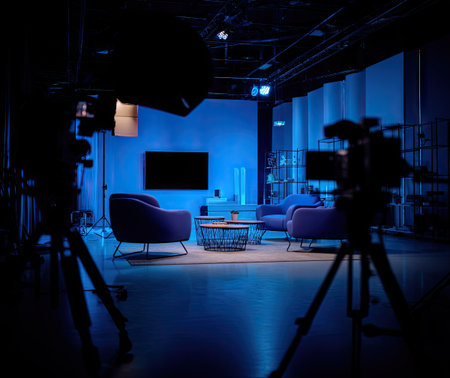 A studio interior is presented with various furniture pieces and camera equipment. The setting features blue lighting, creating a mood. The composition focuses on the arrangement for media production. This setup is suitable for commercial use, offering space for video recording.の素材