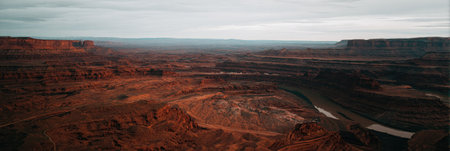 An expansive landscape displays a vast canyon with layered rock formations in earthy tones. The composition presents a wide perspective under a cloudy sky, suggesting a remote environment. The image may serve as a backdrop for various design projects or represent travel and nature concepts.の素材
