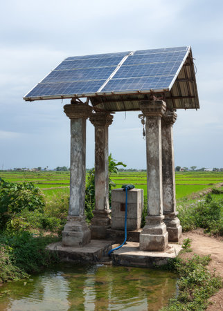 An outdoor scene features a solar panel installation atop an aged, columned structure, likely a well. The composition reveals a blend of architectural elements and nature, with green fields in the background. Natural lighting and an overcast sky suggest a daytime environment. This image could be suitable for articles related to sustainability or energy.の素材