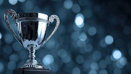 A close-up view presents a silver trophy cup, its surface reflecting light. The background features a soft bokeh effect, creating a sense of depth and focus. The composition emphasizes the trophy's form, suggesting concepts of success and reward. Suitable for various projects related to achievement, awards, and recognition.の素材