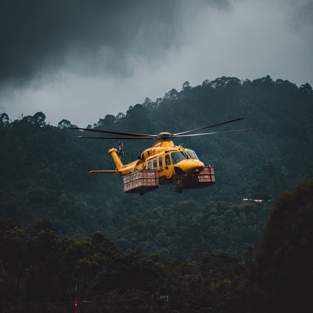 Yellow helicopter transporting cargo, flying over a dense, green forest on a cloudy dayの素材