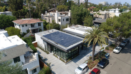 An aerial perspective showcases several modern houses equipped with solar panels. The image presents contemporary architectural designs with clean lines. The composition is bright with natural sunlight, suggesting a daytime scene. Suitable for illustrating themes of sustainable energy, real estate, and urban planning. Potential uses include editorial and commercial projects.の素材