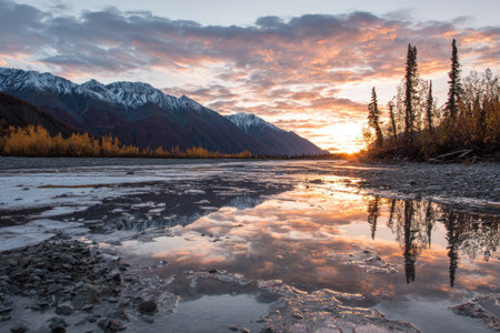 A tranquil landscape captures a scenic view during sunset. The image shows mountains in the distance and a body of water in the foreground, creating a mirror effect. The sky displays vibrant hues with visible clouds. Suitable for diverse applications, including travel and environmental themes.の素材