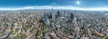 An aerial panoramic view showcases a modern cityscape dominated by skyscrapers and urban structures. The image displays a clear blue sky, buildings, and streets. The visual style features bright, natural lighting. Suitable for a variety of commercial and editorial uses related to business or development themes.の素材