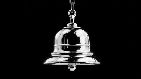 A close-up captures a reflective silver bell hanging from a chain against a solid black backdrop. The bell's glossy surface shows a slight reflection, highlighting its curves and details. The image uses high-contrast lighting to accentuate the metallic texture, suggesting uses for design or editorial projects.の素材