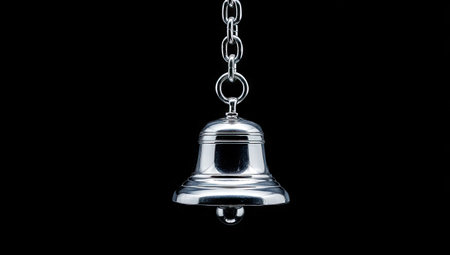 A close-up captures a reflective silver bell suspended from a chain, set against a stark black background. The bell exhibits a polished, metallic texture and gleams under focused lighting. The composition is simple, emphasizing the object's form. This image is suitable for various commercial uses, including advertising and editorial content.の素材