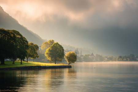 A scenic landscape showcases a calm lake reflecting the sky and surrounding environment. Lush green trees line the shore, contrasted against the subtle hues of mountains in the background. Overhead light illuminates the scene creating a serene atmosphere, possibly suitable for nature-themed projects.の素材