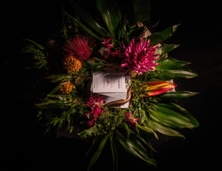 An overhead view reveals a circular floral arrangement centered on a dark backdrop. The composition features diverse blooms in shades of red, orange, and pink, interspersed with lush green leaves. The style suggests a studio setting, emphasizing texture and color, suitable for various design projects and editorial uses.の素材
