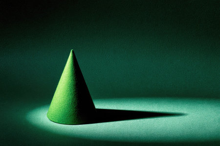 A green cone stands in a spotlight against a deep green backdrop. The object casts a long, distinct shadow. The image uses dramatic lighting to emphasize the shape and texture. This studio shot could be used for various commercial or educational purposes, including abstract concepts.の素材