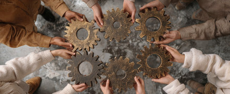 This image showcases multiple hands arranging interconnected gears. The composition features various tones and textures. The overhead lighting suggests an indoor setting. This visual may be suitable for illustrating themes such as collaboration, business development, or technological concepts within diverse applications.の素材