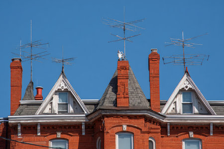 A detailed view of a classic red brick building with multiple chimneys and roof antennas is presented. The composition features a symmetrical arrangement, highlighted against a bright blue sky. This image showcases architectural detail and could be suitable for historical, urban, or construction-related projects. It offers potential use in various commercial and editorial contexts.の素材