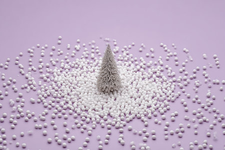 A small, artificial Christmas tree stands centered amidst a sea of white spheres, set against a soft lavender backdrop. The composition features a clean, minimalistic style with neutral colors and soft lighting. This image may be suitable for holiday-themed marketing or website design purposes, emphasizing themes of celebration and decoration.の素材
