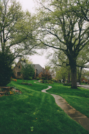 An image captures a house situated amidst verdant surroundings, featuring a winding pathway and lush green lawn. The scene, bathed in soft, diffused light, showcases the textures of grass, trees, and stone. The composition evokes a sense of calm and tranquility, suitable for various editorial and commercial applications related to property or landscapes.の素材