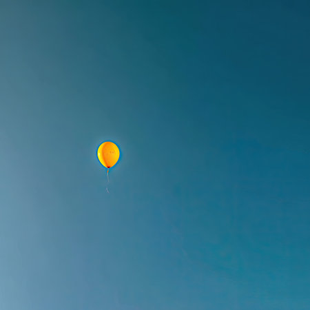 An isolated yellow balloon ascends against a bright blue sky, the focus of the composition. The image exhibits a minimalist style with a clean, unobstructed view, and even lighting. This visual can be suitable for various uses, including design, advertising, and editorial content relating to concepts of freedom or celebration.の素材