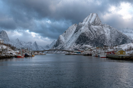 A scenic view captures a mountain range covered in snow, reflected in calm water. A bridge connects structures, with a mix of buildings dotting the shorelines. The scene exhibits a naturalistic style with cool tones and overcast lighting, suitable for landscape or environmental visuals.の素材