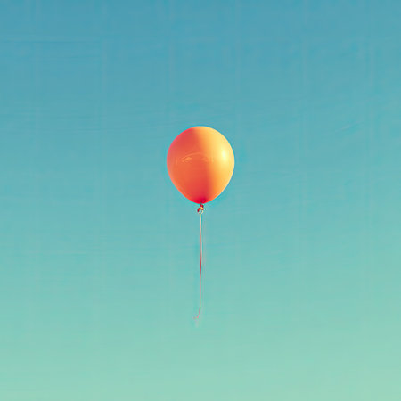 An orange balloon hovers in a clear, azure sky. The image features high contrast with a focus on a single object. Its simple composition creates a feeling of lightness and freedom. This image could be used for various commercial projects related to joy or celebration.の素材