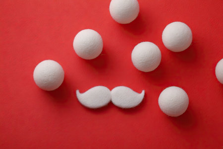 An overhead view displays white spheres and a mustache arrangement set against a vibrant red background. The image showcases simple shapes and contrast with even lighting. This composition is suitable for creative projects, design layouts, and marketing materials seeking a clean, minimalist visual appeal.の素材