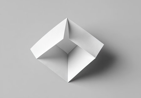 An overhead view displays an abstract geometric form crafted from white paper. The object exhibits sharp folds and angles, creating a three-dimensional effect. The minimalist composition features clean lines and a simple, monochromatic palette against a gray backdrop, suitable for various design projects and visual applications.の素材