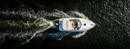 An overhead perspective reveals a white boat cutting through dark water, creating foamy wakes. The composition highlights the vessel's movement, with the sun casting highlights on the water. Suitable for illustrating travel, leisure, or transportation concepts, this image offers potential for diverse commercial applications.の素材