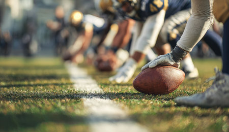 An American football game features players lined up. A close-up showcases the ball on the grass field. The composition includes focus on hands and gloves, green field and a blurred background. This dynamic image could be used for sports articles or commercial promotions.の素材
