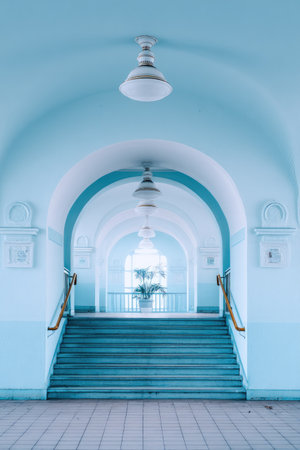 A long hallway with arched ceilings and a staircase dominates the composition. The cool, light blue tones create a serene atmosphere. Overhead lights illuminate the space. The image could be used for architectural concepts, interior design, or adding a sense of depth to various visual projects.の素材