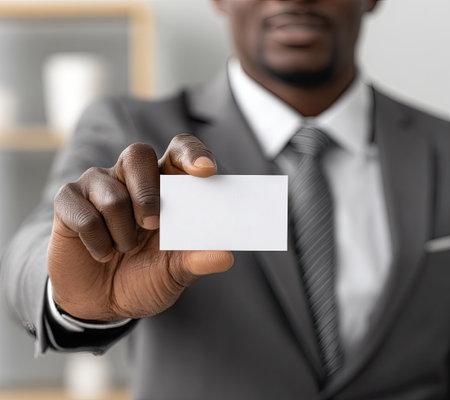 A close-up captures a man in a professional suit presenting a blank business card. The composition features soft lighting and focus on the card and hand. It suggests a corporate or business setting, offering potential use for promotional material or business presentations.の素材