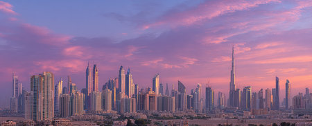 A cityscape is silhouetted against a colorful evening sky, showcasing numerous skyscrapers and other buildings. The scene displays a mix of architectural structures with a warm light and a soft, pink, and purple sky. Suitable for use in various commercial applications, including stock photography and visual content.の素材